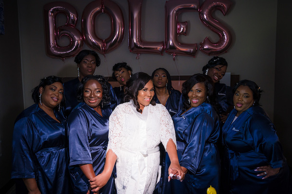 bride in a white robe standing with her bridal party dressed in Navy blue robes