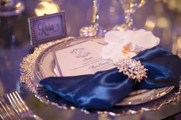 silver charger plate with navy blue satin napkins, custom menu card and a rhinestone napkin ring