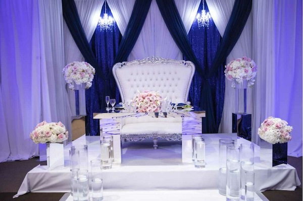 Sophisticated sweetheart table with luxurious blush floral arrangements, floating candles and blue and white draping