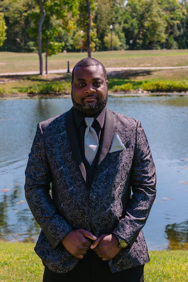 groom standing next to a pond wearing a luxurious patterned tuxedo jacket