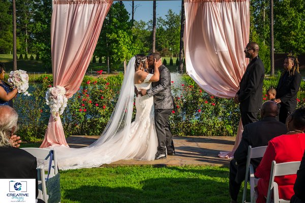 bride and groom kissing under a pink satin draped wedding arch at Doko Manor in Blythewood South Carolina