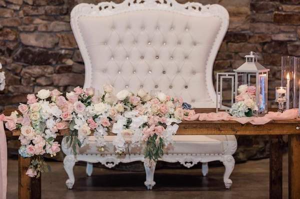 white tufted loveseat behind a rustic farmhouse table with blush and white flowers