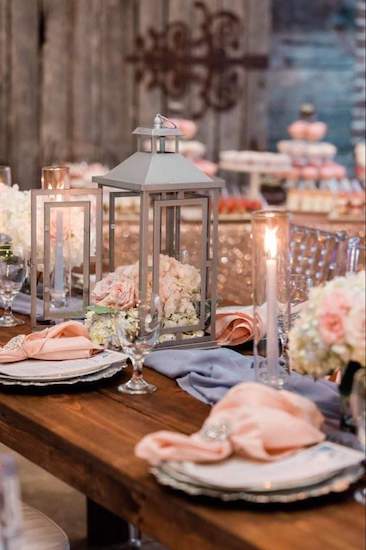 tablescape of blush napkins and flowers with lanterns and dusty blue fabric runner