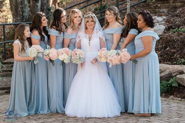 bride and her bridal party wearing dusty blue dresses carrying blush and white flowers